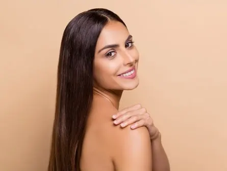 Stock photograph of a model: a smiling woman with long dark hair looks back over her bare shoulder against a beige backdrop