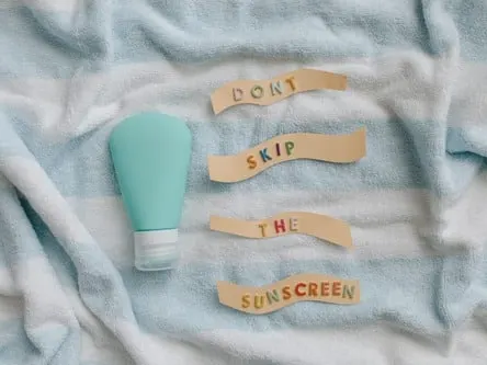Stock photograph: a teal sunscreen bottle on a striped towel beside paper strips spelling "Don’t skip the sunscreen"
