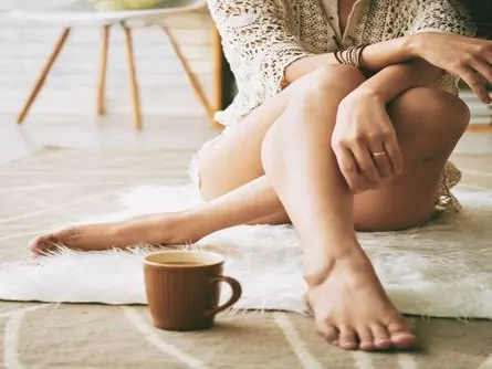 Stock photograph of a model: a barefoot woman in a lace top sits on a fur rug with her legs crossed beside a mug