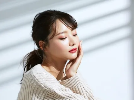 Stock photograph of a model: a young woman with a ponytail rests her hand against her cheek in soft window light