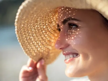 Stock photograph of a model: a smiling woman in a straw sun hat with dappled sunlight across her face