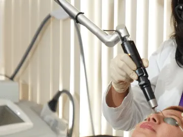 Dr. Nita Patel, in protective glasses, treats a patient’s face with a laser in her office
