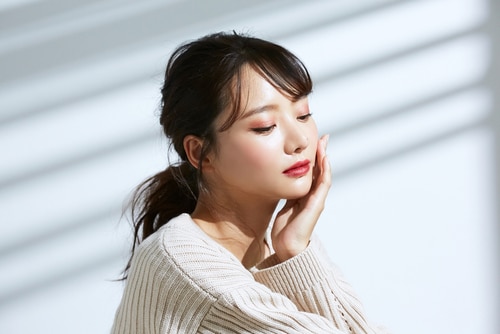 Stock photograph of a model: a young woman with a ponytail rests her hand against her cheek in soft window light