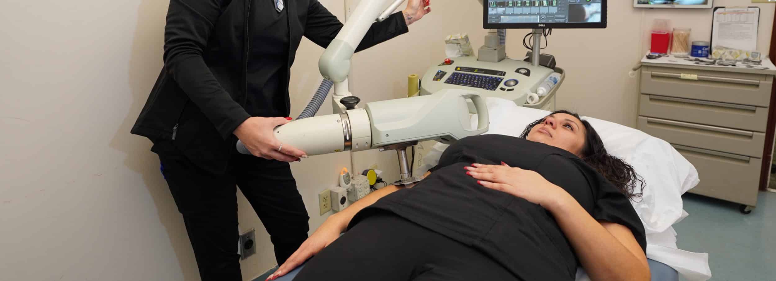A staff member in black positions a superficial radiation therapy unit over a patient lying on an exam table