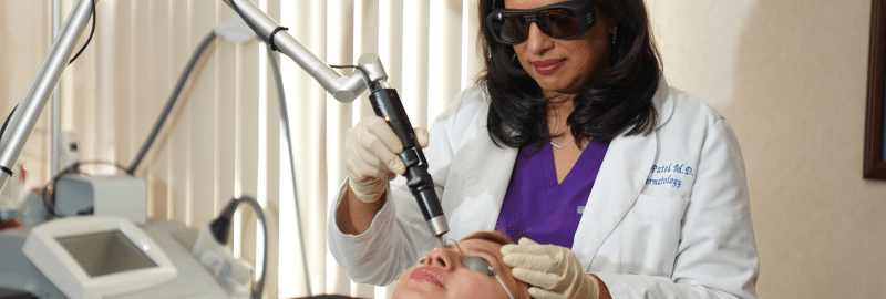 Dr. Nita Patel, in protective glasses, treats a patient’s face with a laser in her office