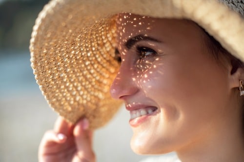 Stock photograph of a model: a smiling woman in a straw sun hat with dappled sunlight across her face