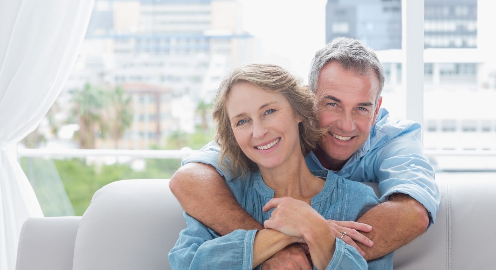 Stock photograph of models: a smiling couple embracing on a sofa in a bright room