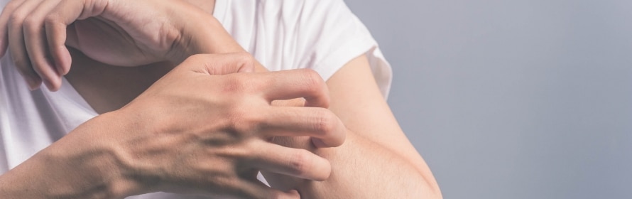 Stock photograph of a model: a person in a white shirt scratching their forearm with the other hand, against a grey background.